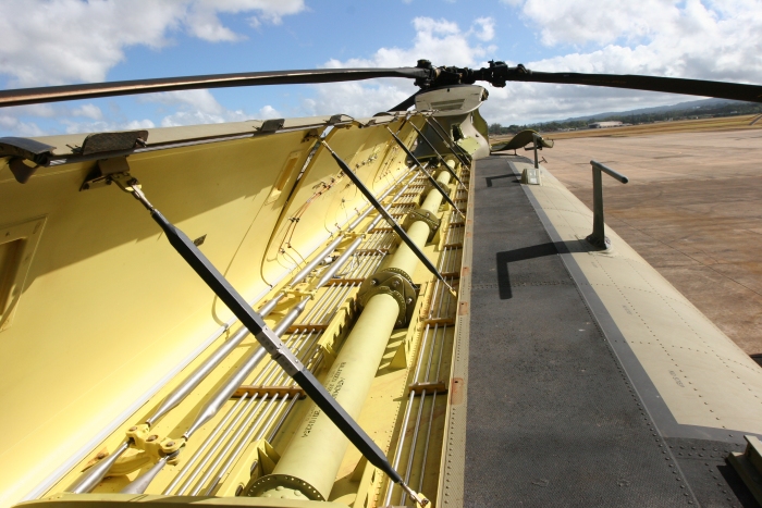 The top of the CH-47F looking forward from the Combining Transmission area with the Tunnel Covers open. The Synchonizing Drive Shafts, shafts 2 thru 6 of the 7 forward of the Combining transmission are visible here. These shafts keep the Forward and Aft Rotor Systems in phase by locking the Forward, Combining and Aft Transmissions together. When one transmission turns, so will the others. While in phase, the Rotor Blades from each head do not touch or overlap each other. If they touch in flight the aircraft will disintegrate within seconds.