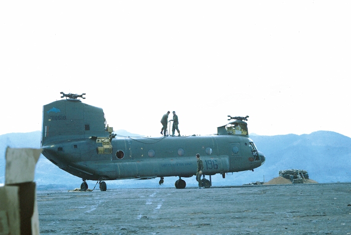 Two soldiers stand ready on the top of 67-18518 to attach the sling to the cargo hook of 68-15869 awaiting nearby.